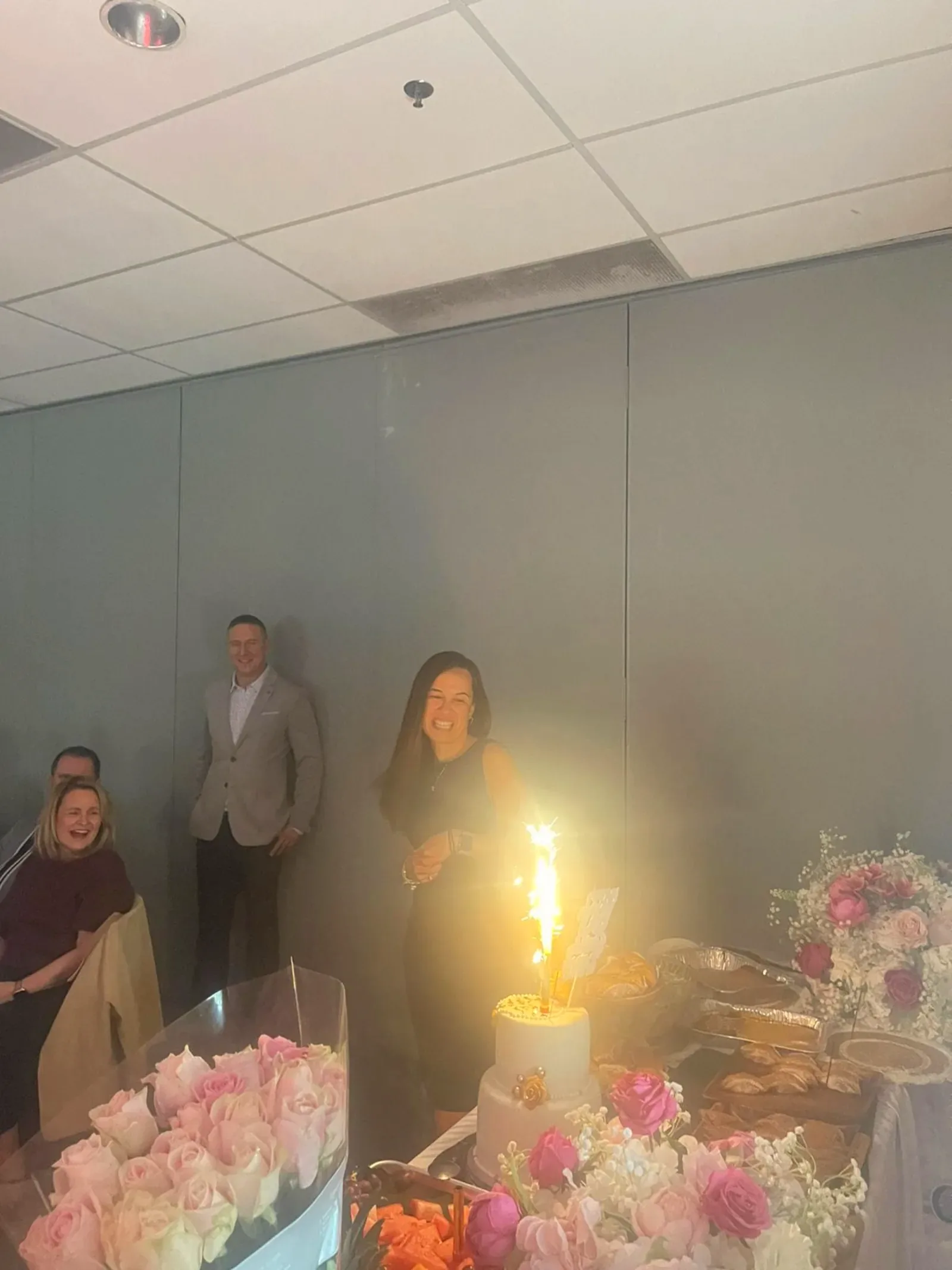 A guest laughing as a sparkler candle blazes on a tiered cake surrounded by roses at a 50th birthday