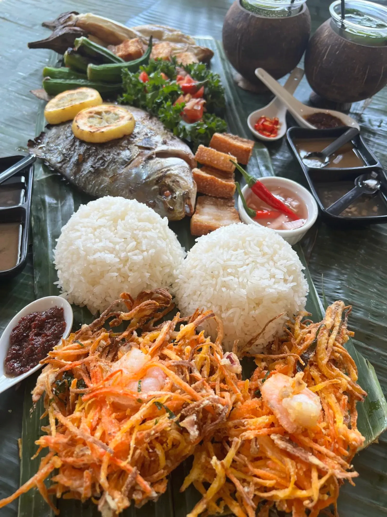 Kamayan feast — whole grilled fish, lechon kawali, ukoy fritters, rice mounds and dipping sauces on banana leaves